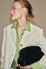 Bolso de mano tipo sobre con diseño trenzado y acabado efecto acharolado. Cuenta con cierre imantado, bolsillo interior con cremallera y detalle de borla lateral con pieza metálica.
