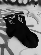 Medias negras de algodón con logo de alas bordado en blanco y detalle de doble línea blanca en el borde superior.