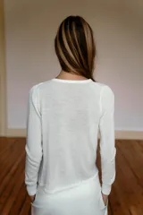 Jersey de punto fluido color blanco, con cuello redondo, manga larga y detalle de pliegues drapeados en el hombro.