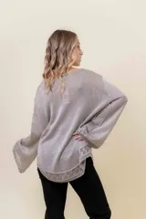 Sweater de tejido liviano con efecto lurex, color beige o gris claro metalizado. Presenta cuello redondo, mangas amplias estilo campana y terminaciones en punto elástico con diseño de cuadros en puños y ruedo.