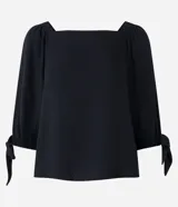 Blusa negra de viscosa con escote off-shoulder, mangas 3/4 con elásticos y lazos en los puños.