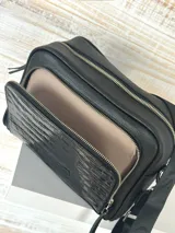 Bandolera negra de cuero con textura tipo cocodrilo en la parte superior. Tiene correa de tela negra con letras blancas y herrajes plateados.