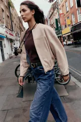 Campera bomber color beige, de cuello redondo y manga larga. Tiene bolsillos delanteros y bajo acabado en elástico. Cierre frontal con cremallera.