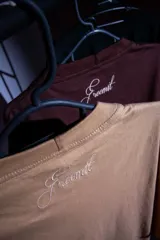 Remera color arena con cuello redondo y estampado frontal con letras "MTPE" en marrón.