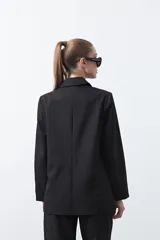 Blazer sastrero negro de doble botonadura con botones marrones, cuello solapa y mangas tres cuartos. Tiene dos bolsillos delanteros con solapa.