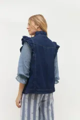 Chaleco de denim azul con estampado paisley, sin mangas, con volados en hombros y cuello, cierre frontal con botones metálicos y bolsillos laterales.