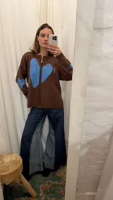 Campera tejida en hilo color crudo con diseño de corazón negro central, cierre frontal completo y detalles bordados en rojo y negro en mangas y cuerpo.