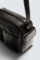 Bandolera de cuero color marrón oscuro con diseño estructurado. Cuenta con un compartimento principal con cierre de cremallera, dos bolsillos frontales con cierre de botón a presión y bolsillos laterales adicionales. Incluye un asa de hombro ajustable.