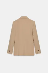 Blazer cruzado color beige, de manga larga, con cuello solapa y forro interior negro. Presenta cierre frontal con botones dorados y bolsillos de vivo en el pecho y bolsillos con solapa en el delantero.