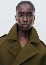 Chaqueta corta de doble botonadura en color verde militar, con cuello de solapa, bolsillos laterales, trabillas en los hombros y mangas largas con puños abotonados.