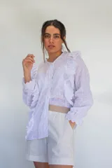 Camisa blanca de algodón estilo romántico con tejido broderie, mangas largas con puños volados y detalles de volados frontales.