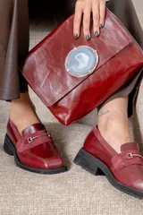 Mocasín de cuero vacuno color bordó, con detalle de gamuza en la capellada, herraje metálico plateado y suela de goma negra con taco bajo.