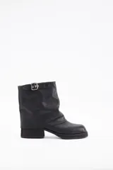 Botin de cuero vacuno color negro, con diseño de caña media holgada y detalle de tira con hebilla metálica en la parte superior. Presenta punta cuadrada y taco bloque bajo.