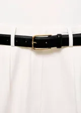 Mono largo de diseño recto y estilo minimalista, color blanco. Presenta cuello perkins, sin mangas con tirantes anchos, detalle de pinzas delanteras y cierre de cremallera en la parte posterior. Incluye bolsillos laterales y un cinturón negro con hebilla metálica.