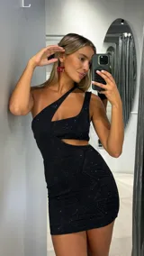 Vestido corto negro de un solo hombro con diseño cut-out en la cintura y detalle de bretel asimétrico. Confeccionado en tejido con sutil brillo y estampado geométrico.