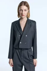 Blazer cropped de sarga con diseño a rayas verticales, corte entallado y cierre frontal cruzado con botones. Presenta detalles desflecados en los hombros y en el canesú trasero, además de flecos de seda desmontables en la solapa.