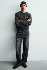 Sudadera de corte relajado, color negro con efecto lavado, cuello redondo y manga larga. Presenta un pequeño estampado frontal con texto en tonos naranja y amarillo.