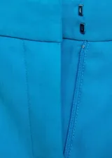 Pantalon de vestir color turquesa, de corte recto y tiro medio, con cierre frontal de botón y cremallera, y bolsillos laterales.