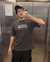 Remera de algodón con efecto lavado stone wash, de corte oversize y manga corta. Presenta un diseño gráfico estampado en la espalda con tipografía artística y texto alusivo a la cultura de barrio.