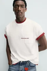 Camiseta blanca de corte relajado (relaxed fit) con cuello redondo y manga corta. Presenta un bolsillo plastrón en el pecho y un estampado de texto en color marrón rojizo en la espalda que dice "SOMETIMES SÍ, SOMETIMES BYE" (reemplazando la 'O' de 'SOMETIMES' por un corazón).