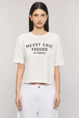 Remera Kosiuko de algodón color blanco, de corte regular y mangas cortas hasta el codo. Cuenta con un diseño estampado en el frente con la leyenda "Messy Chic Kosiuko St. Tropez".