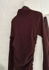 Vestido corto de manga larga en color bordó, con cuello alto y diseño ajustado con frunces laterales que recorren toda la prenda.