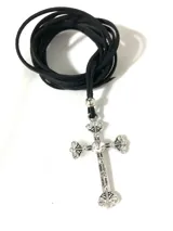 Collar con dije de cruz gótica plateada con strass, colgando de un cordón de cuero sintético negro.