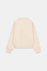 Jersey de punto con cuello tipo polo, manga larga con puños y cierre frontal con botones. Presenta un bolsillo de plastrón en el pecho y diseño de corte holgado.