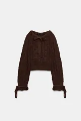 Jersey de punto calado color marrón, con cuello redondo ajustable mediante lazada y mangas largas con puños ajustables con lazos.
