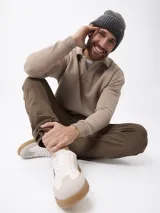 Sweater de felpa color beige, con cuello polo y cierre frontal parcial, de manga larga con puños acanalados.