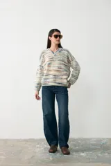 Sweater de punto con diseño oversize y cuello en V, tejido en tonos crudo con rayas horizontales multicolores.