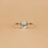 Anillo solitario de oro blanco 18k con una piedra central de aguamarina en corte ovalado y pequeños brillantes laterales engarzados en cuatro puntas.