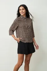 Camisa de manga tres cuartos con estampado de leopardo en tonos beige y negro, cuello camisero y botones frontales.
