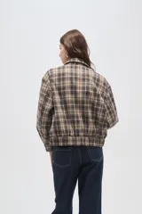 Chaqueta de estilo camisa a cuadros en tonos beige y marrón, con cierre frontal, cuello camisero y capucha integrada. Presenta un diseño holgado y mangas largas.