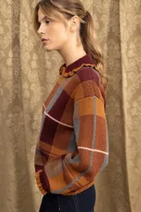 Campera de punto con diseño a cuadros tartán en tonos marrones y beige. Presenta un corte oversize, cierre frontal con cremallera, cuello tipo babero con volados y mangas largas con puños ajustados.