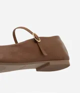 Zapatilla plana de cuero marrón estilo Mary Jane, con puntera cuadrada y tira fina con hebilla metálica dorada sobre el empeine.