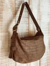 Bolso de hombro tipo hobo con acabado texturizado efecto craquelado en tonos beige y blanco. Cuenta con una correa ajustable con hebilla metálica, cierre superior y diseño espacioso.