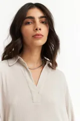 Blusa negra de manga larga con cuello tipo polo y escote en V. Presenta un diseño holgado con textura sutil en la tela y puños abotonados.