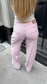 Pantalón de tiro medio confeccionado en tela jersey rib color rosa, con diseño de pierna ancha y bolsillos laterales. Presenta costuras visibles en hilo de color contrastante.