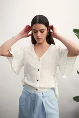 Camisa negra con botones dorados, escote en V y mangas cortas amplias con lazos laterales. 