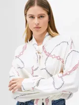 Blusa blanca hueso con estampado de cadenas en tonos negro y rosa, cuello alto con lazada ancha integrada, corte regular y manga larga.