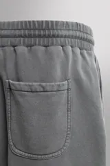 Short tipo jogger de algodón con interior afelpado, cintura elástica ajustable con cordón, bolsillos frontales y bolsillo trasero. Presenta un efecto lavado y estampado gráfico a contraste en el frente.