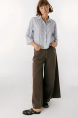 Camisa de algodón color azul claro con rayas verticales blancas y bordado calado de flores blancas. Tiene cuello clásico, cierre frontal con botones y mangas 3/4 acampanadas.