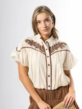 Blusa de algodón color off white con cuello mao, canesú con detalles de broderie y bordados, mangas cortas abullonadas tipo globo y cierre frontal con botones.