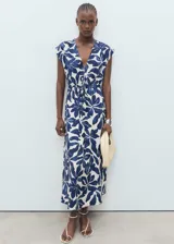Vestido largo de corte evasé con estampado botánico en azul y blanco. Presenta cuello de pico, mangas cortas y un panel fruncido en la cintura con cordón ajustable.