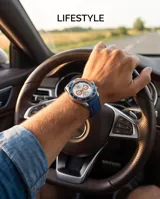Reloj de pulsera analógico con cronógrafo, caja de metal y correa de caucho azul. Presenta esfera blanca con detalles en naranja y bisel giratorio azul.