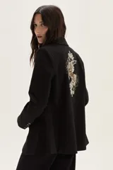 Blazer negro de corte clásico con cierre frontal de botones y detalle de bordado artístico en la espalda que representa un caballo y motivos florales.