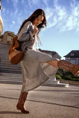 Mochila tipo bucket color marrón tostado, confeccionada en gamuza con detalles en cuero color beige. Cuenta con bolsillo exterior con cierre, bolsillo interior con cierre, llavero interno, asa de mano y correa extraíble y regulable para usar como mochila o bolso de hombro.