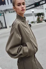 Cazadora estilo bomber color gris, con cuello subido, manga larga, bolsillos delanteros de vivo y cierre frontal con cremallera. Presenta bajo ajustable con cordones elásticos laterales.