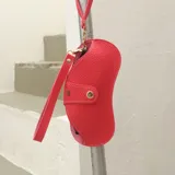 Estuche para lentes de diseño ergonómico y minimalista, confeccionado en cuero sintético con textura granulada. Cuenta con cierre magnético frontal, costuras a la vista en color contrastante y una correa de mano extraíble.